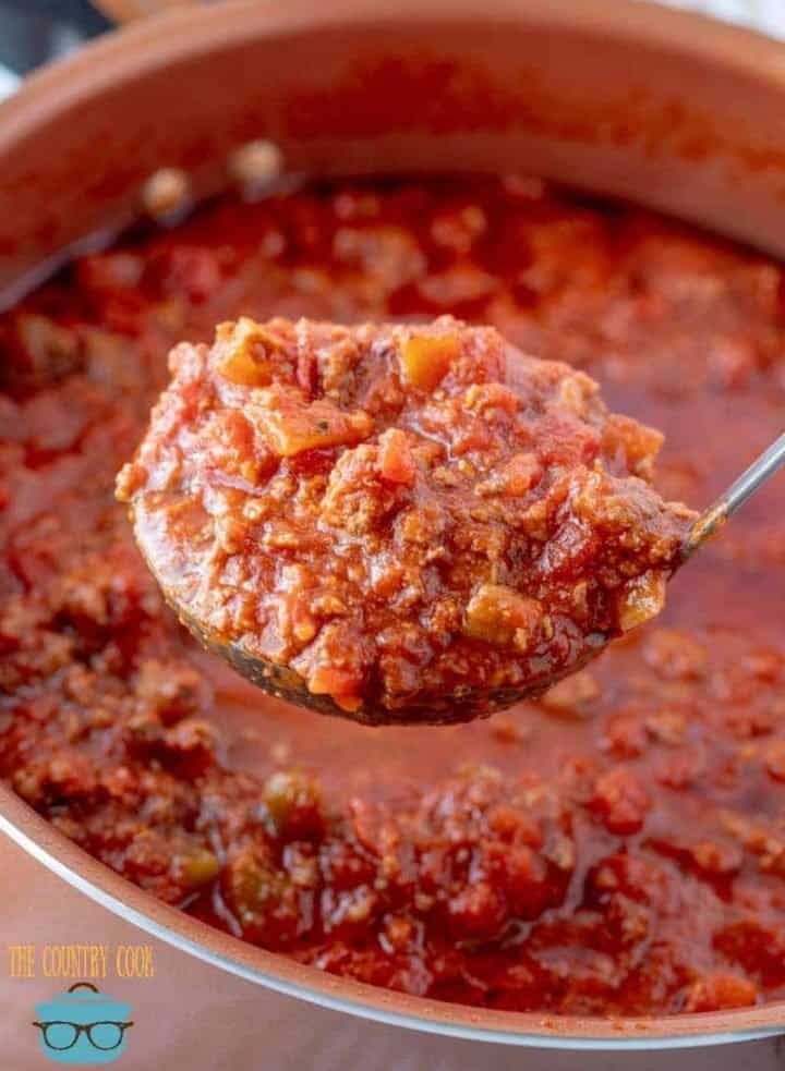 a sauce spoon holding up beefy spaghetti sauce over a pot.