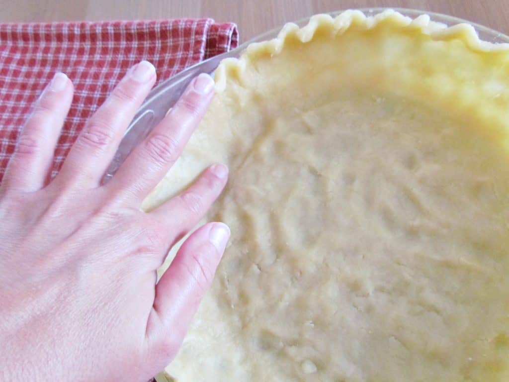 finger pressing the inner bottom corner of the pie crust to thin it out. 