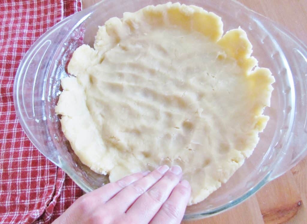 hand shown pushing the dough to the sides of the pie pan.
