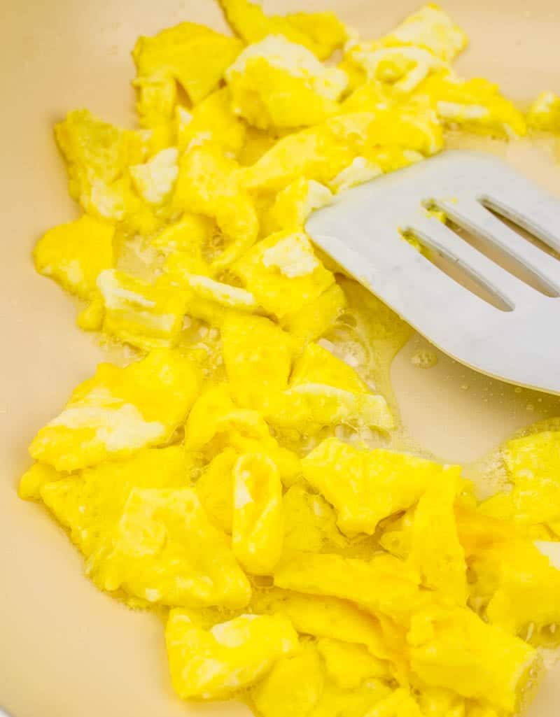 scrambled eggs in a large skillet with a white spatula.