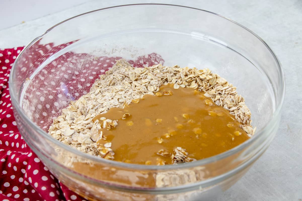 peanut butter mixture poured over oat mixture in a clear bowl.