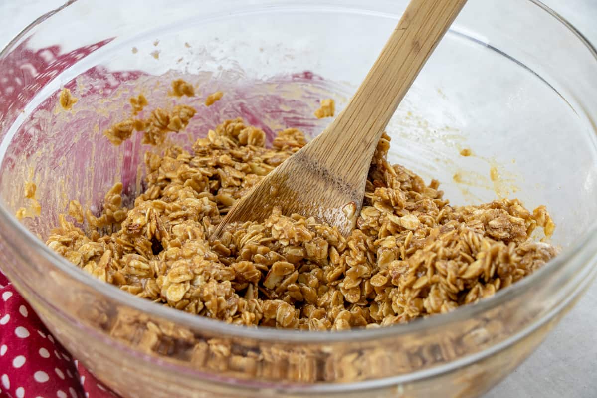 stirring granola mixture together in a bowl with a wooden spoon