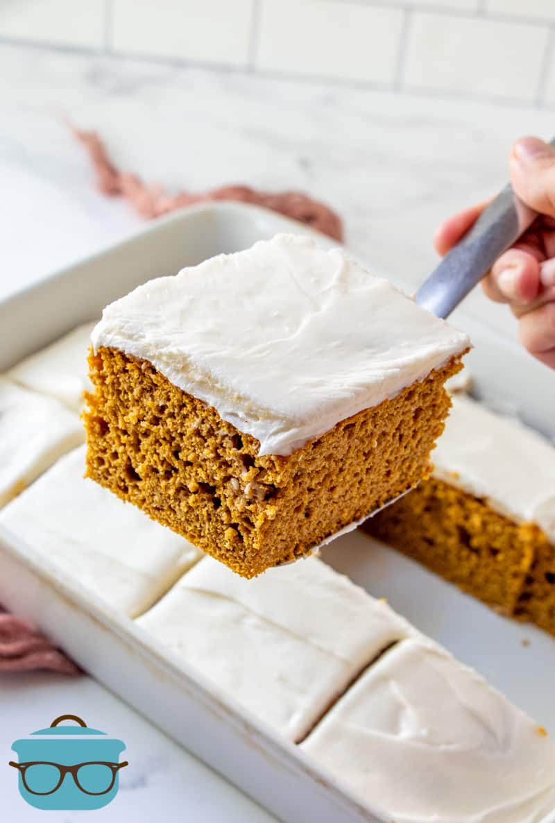 sliced pumpkin spice cake in a baking dish, one slice shown raised above the cake on a spatula.