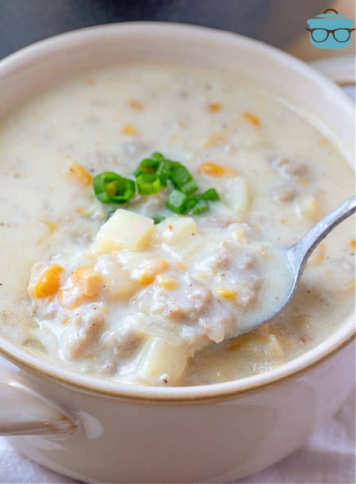 A white bowl filled with corn chowder with sausage and a spoon scooping up some of the soup.