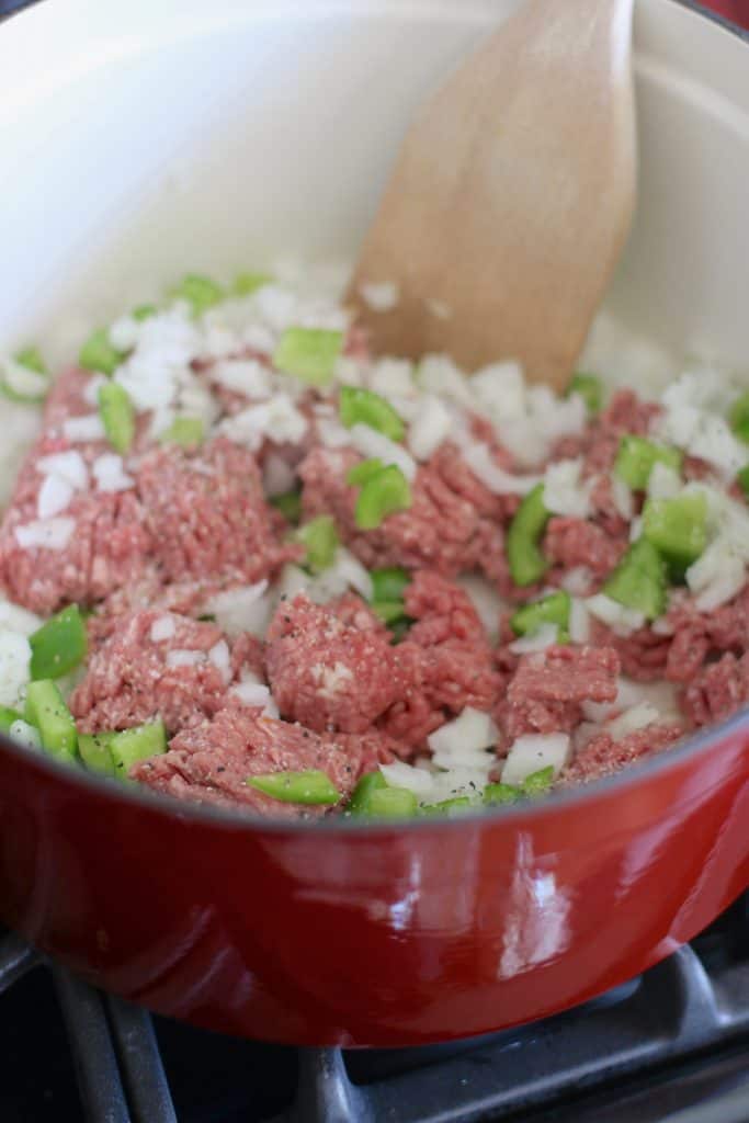 ground beef, green pepper, diced onions in a red dutch oven.