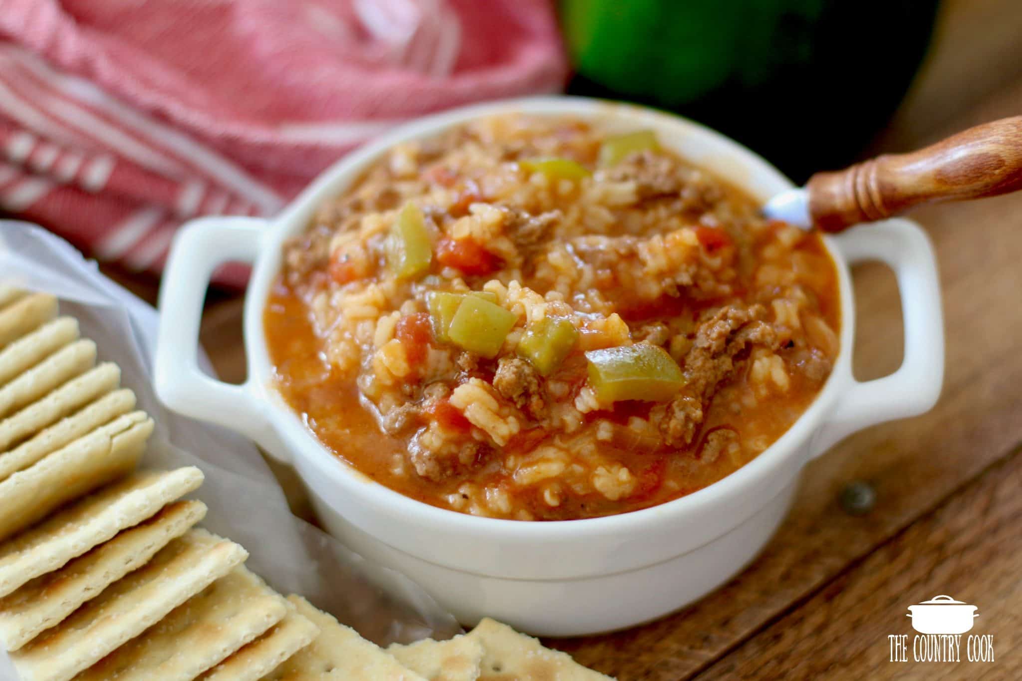 Stuffed Pepper Soup with rice shown in a small white ramekin with a spoon and crackers on the side. 