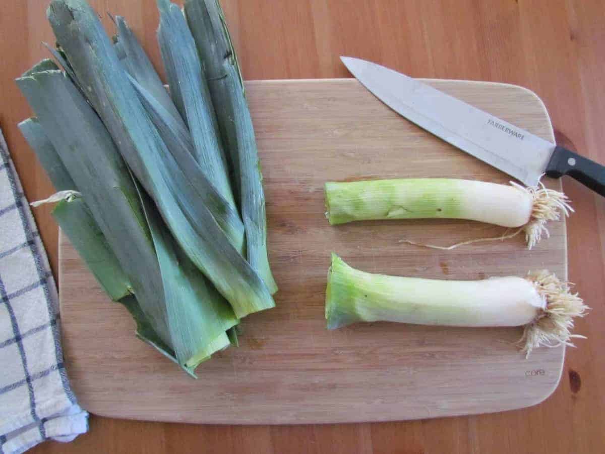 how to cut leeks, leeks shown cut in half on a cutting board.