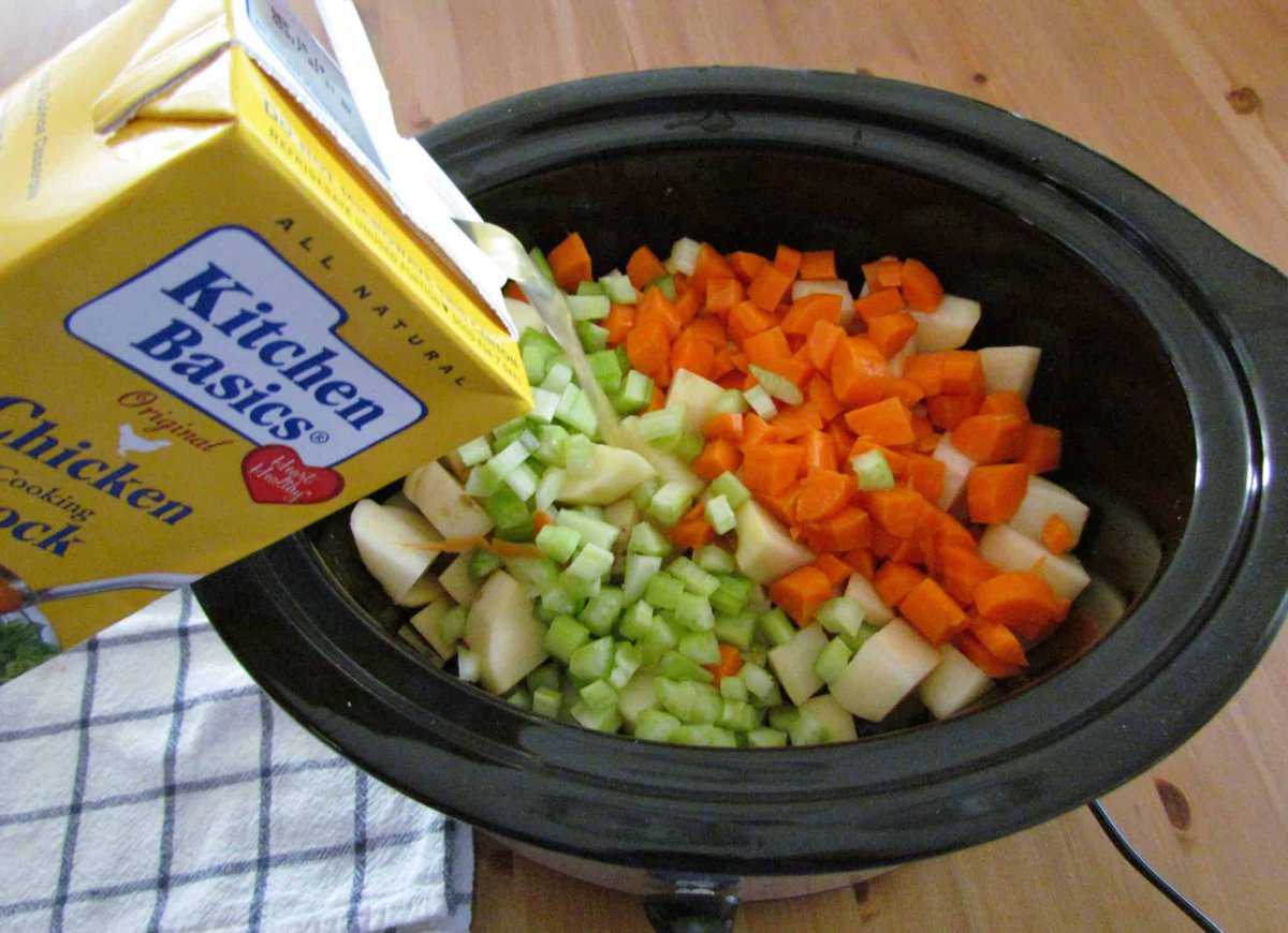 pouring Kitchen Basics chicken stock into slow cooker with diced vegetables.