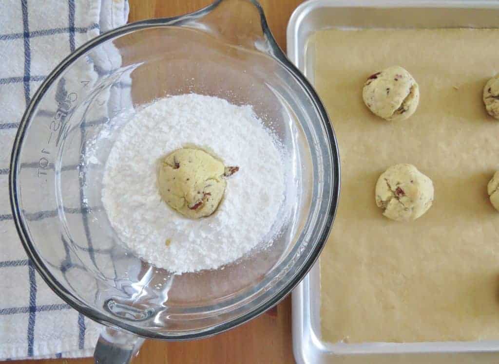 cookie dough ball shown rolling in powdered sugar.