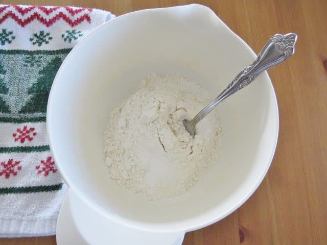 flour, baking soda and salt being mixed together by a fork in a white bowl.