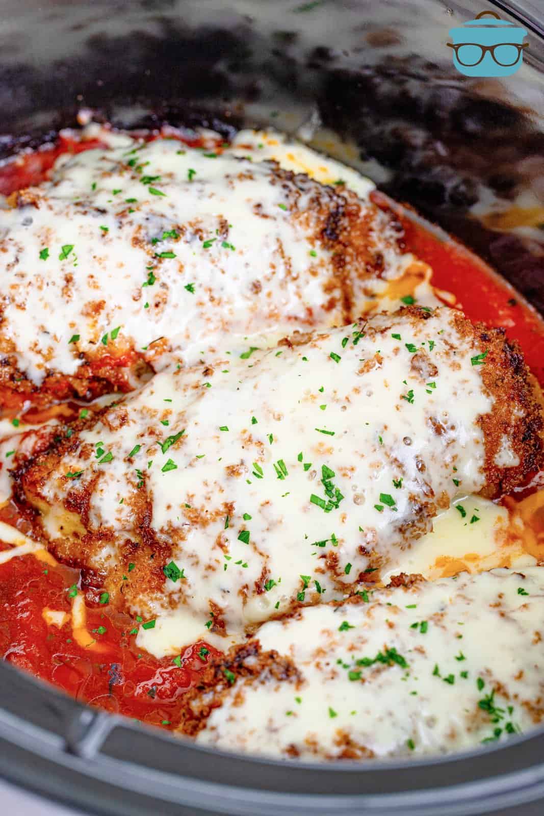 fully baked chicken parmesan in slow cooker with melted cheese on top.