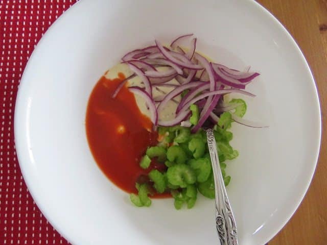 mixing buffalo wing sauce, sliced red onion, sliced celery and ranch dressing a white bowl.