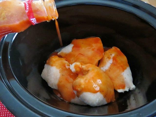 pouring buffalo wing sauce over frozen chicken breasts in the slow cooker.