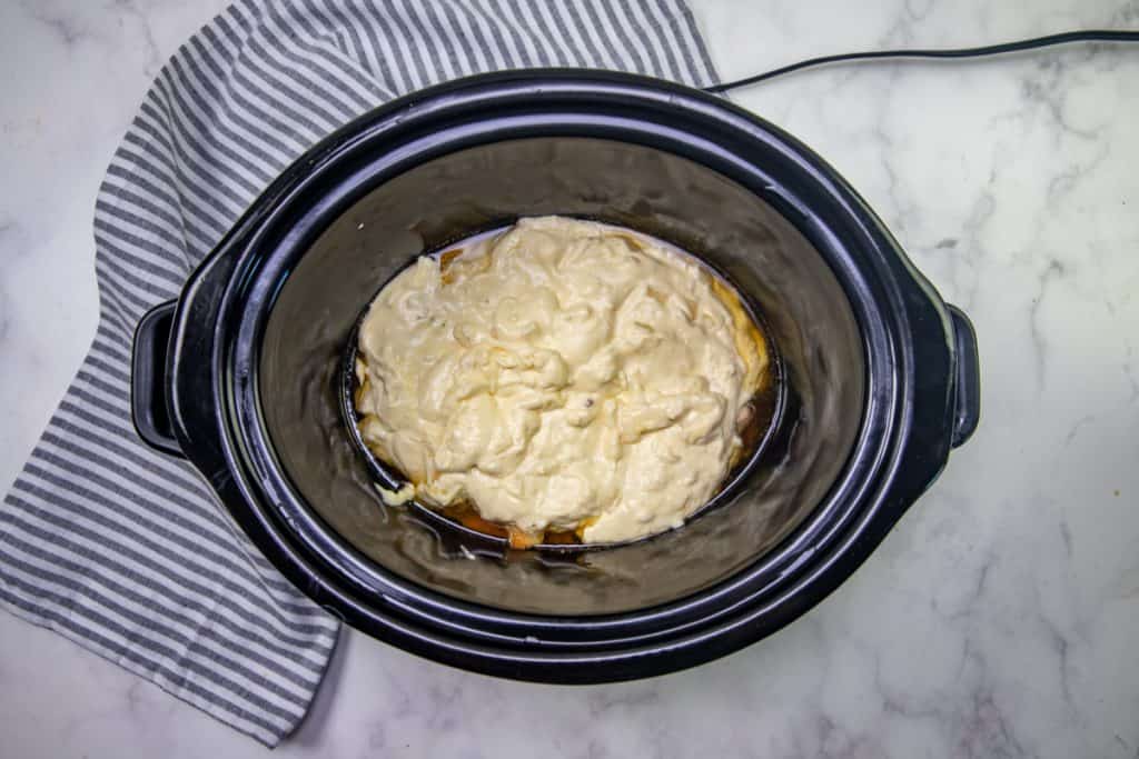 cream mixture added to cooked chicken mixture in black oval slow cooker.