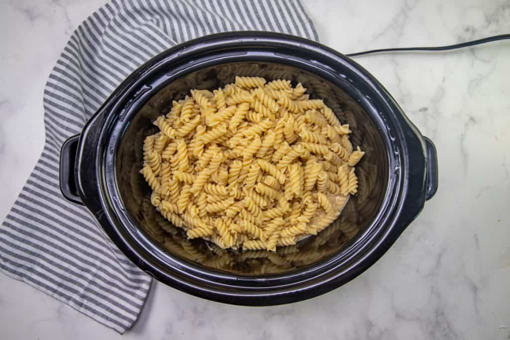 cooked rotini pasta added to creamy chicken mixture in slow cooker.