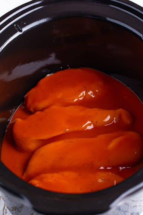 Buffalo sauce covered chicken breast in a crock pot.