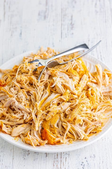 Shredded buffalo chicken on a plate with tongs.