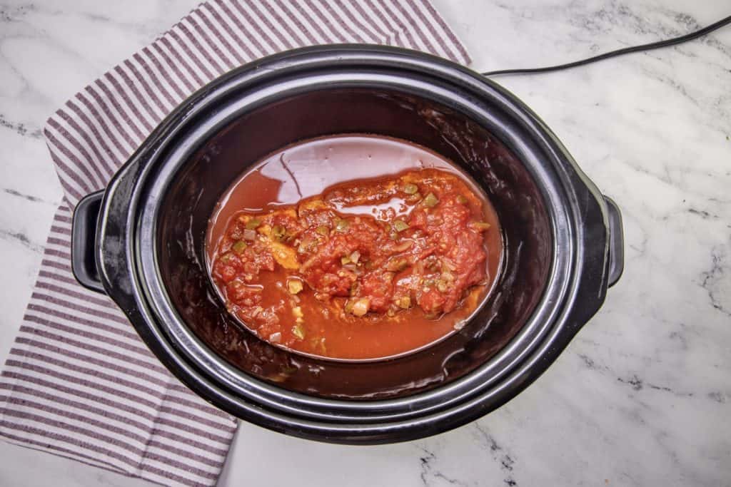 salsa and water covering a chuck roast in a slow cooker.