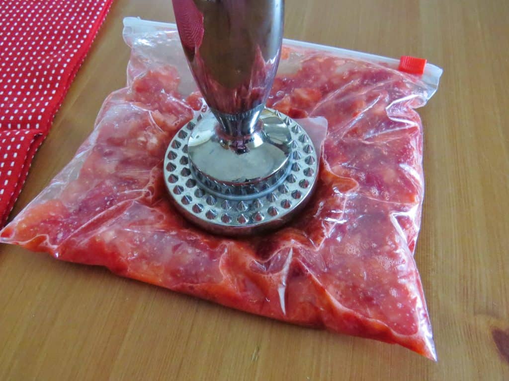strawberries being smashed by a meat tenderizer in a clear Ziploc bag 