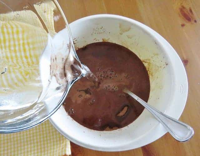 pouring hot water into cocoa in a white bowl