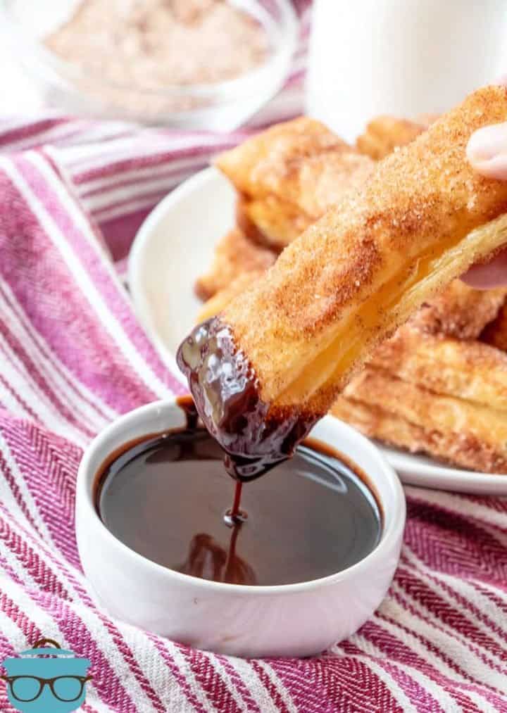 a hand dipping a baked churro into chocolate sauce.