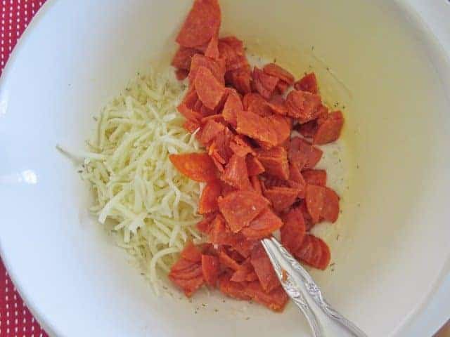 shredded cheese and diced pepperoni slices added to batter in a bowl