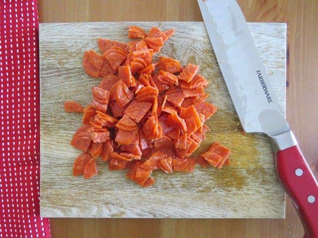 slices of pepperoni shown on a wooden cutting board with a knife set to the side