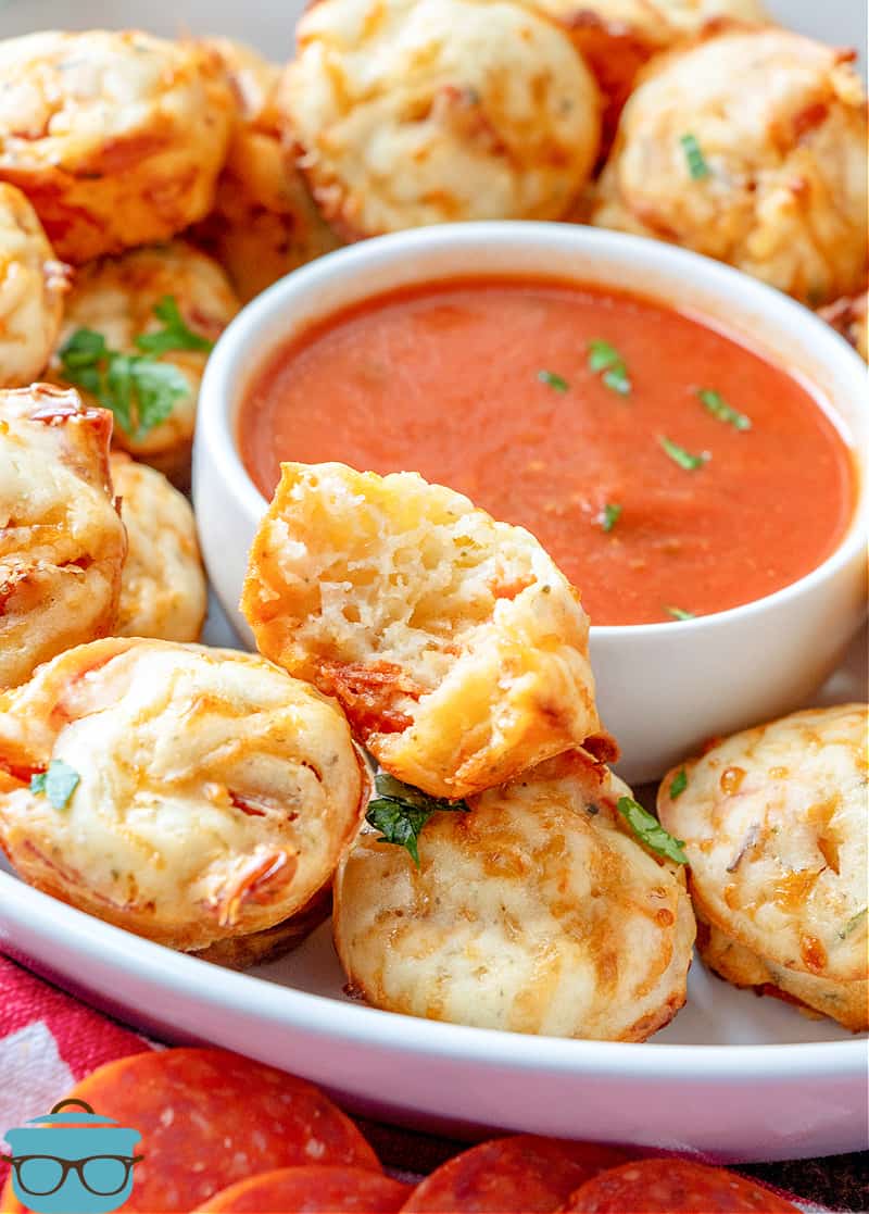 pepperoni pizza puffs shown on a round white plate with a small bowl of marinara sauce in the middle.