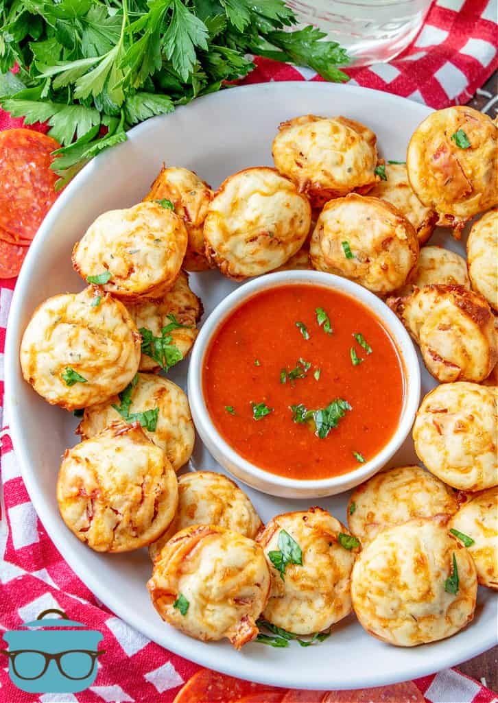 pepperoni pizza puffs shown on a white platter with a small bowl of marinara in the middle of the platter