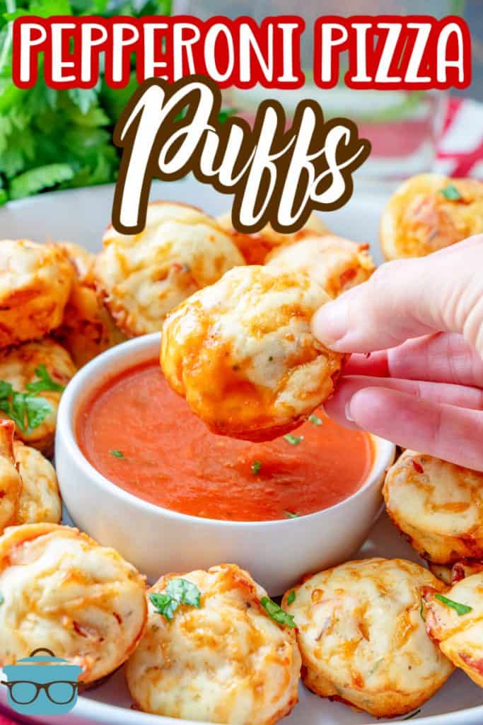 Pepperoni Pizza Puffs recipe from The Country Cook, hand holding one puff and dipping it into a bowl of marinara sauce