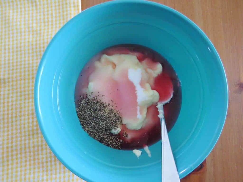 homemade dressing of mayonnaise, red wine vinegar, sugar, pepper stirred together with a spoon in a plastic blue bowl