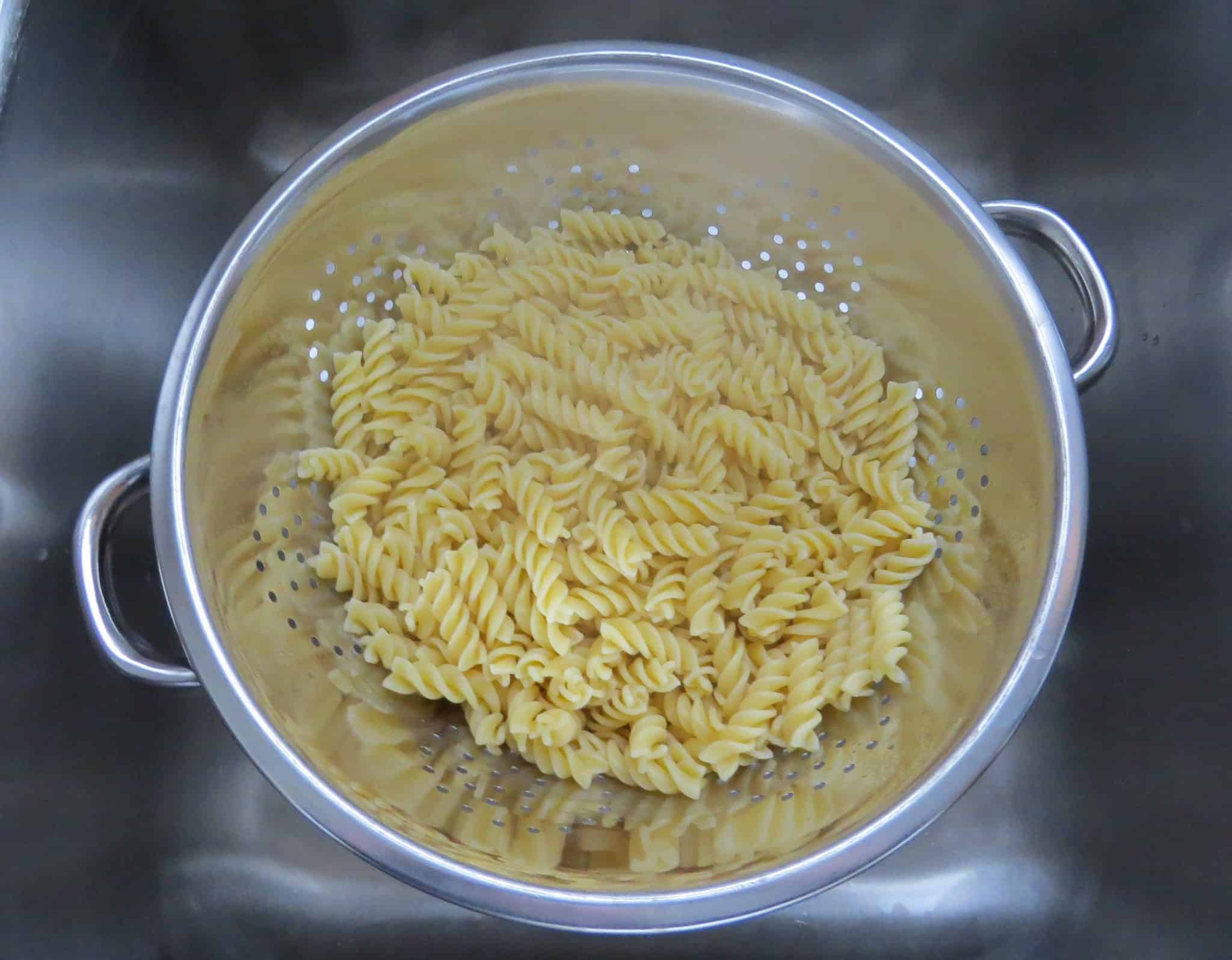 draining excess water from rotini pasta in a metal strainer.
