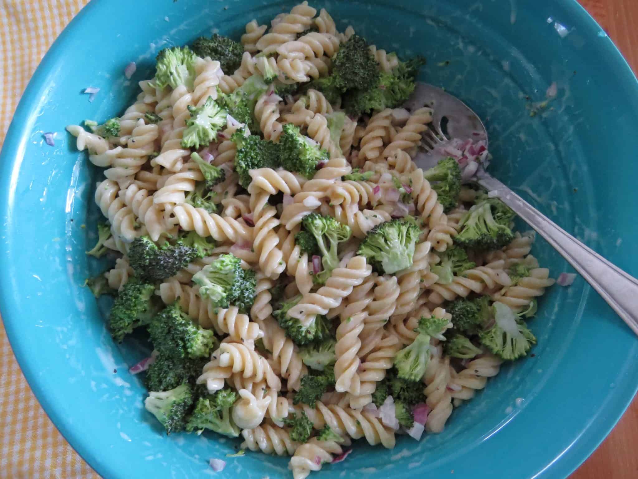 pasta salad being mixed together in a blue bowl.