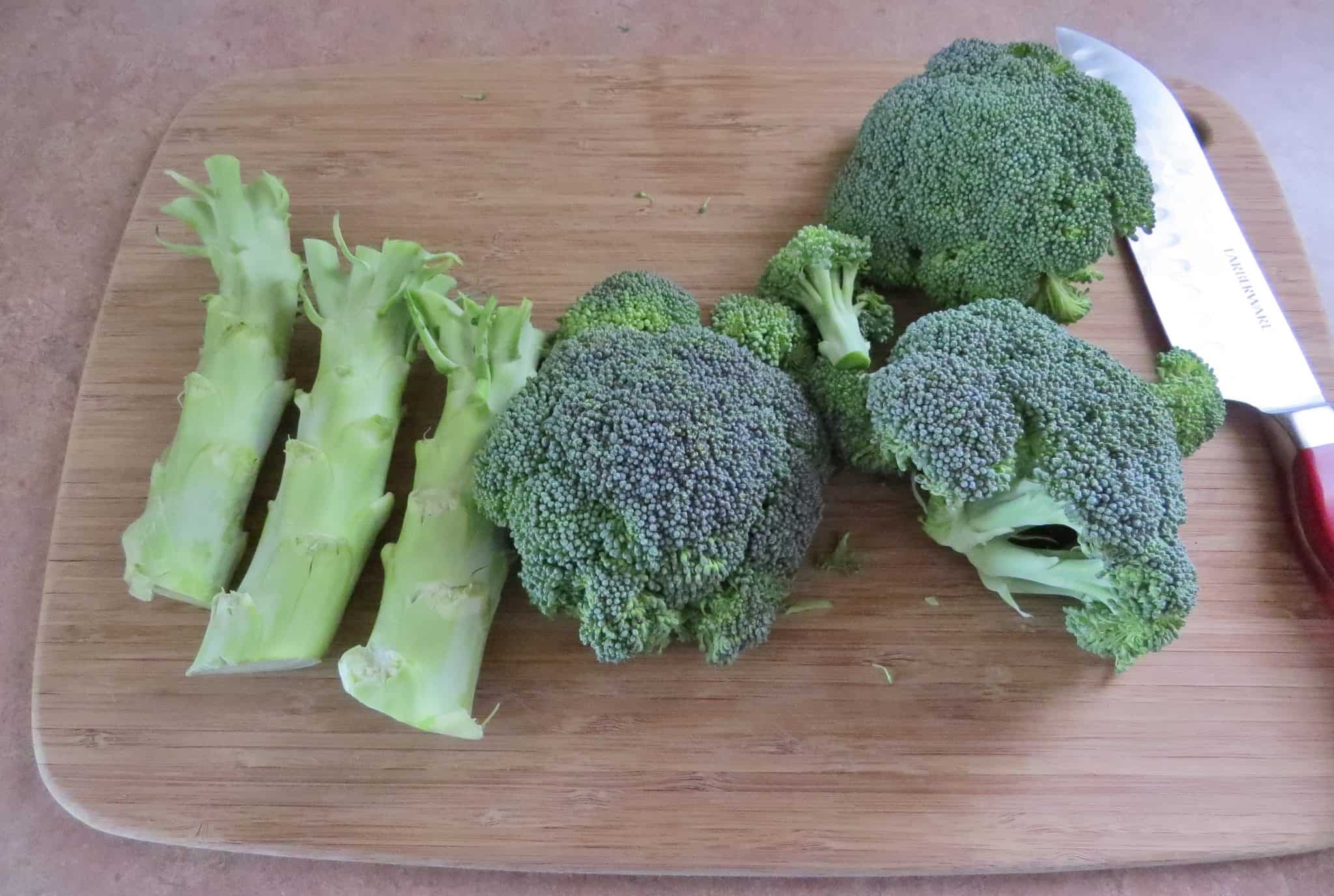 how to chop broccoli, remove florets from the stem, displayed on a wooden cutting board with a chef's knife.