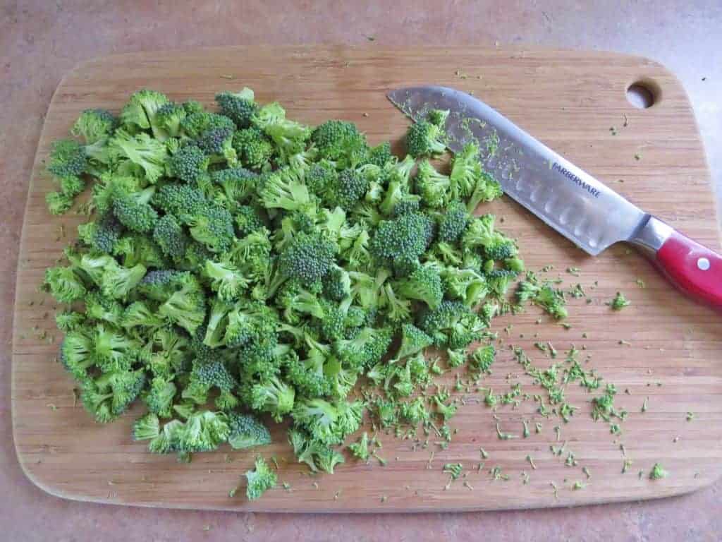 chopped fresh broccoli florets on a wooden cutting board with a chef's knife