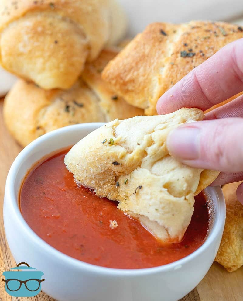 a hand holding a Pepperoni Roll Ups dipped into pizza sauce.