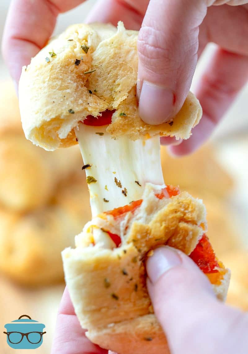 a hand pulling apart a pepperoni rollup to show the melted cheese.