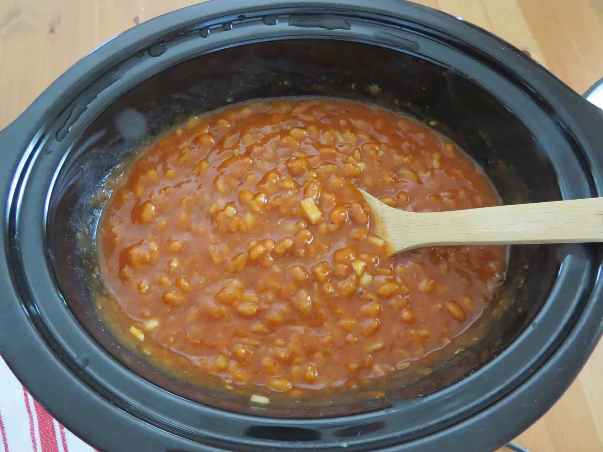 a wooden spoon shown stirring baked beans.