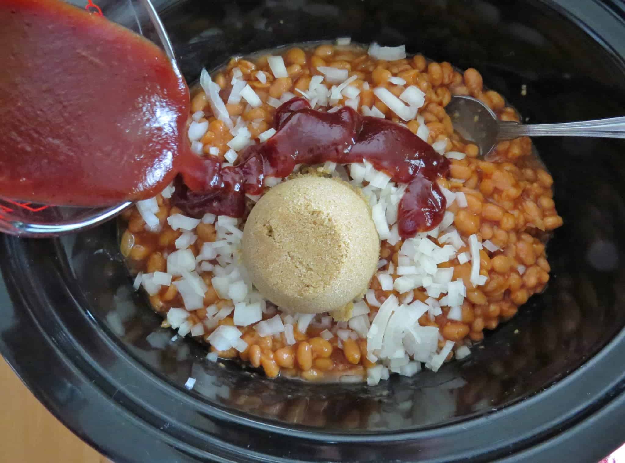 barbecue sauce shown being poured in a crock pot with pork and beans.