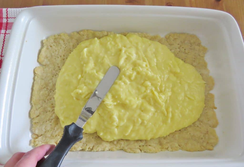 coconut cream pie filling being spread on top of cooked and cooled pie crust in white baking dish