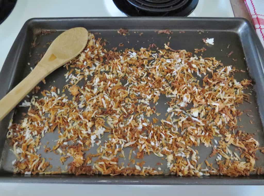 coconut fully golden brown and toasted on a cookie sheet and a wooden spoon