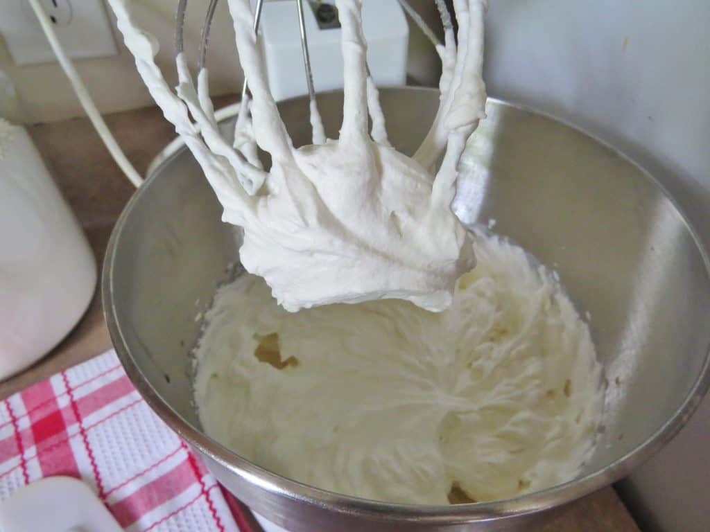 sugar and vanilla added to fresh whipped cream in a stand mixer with whisk attachment