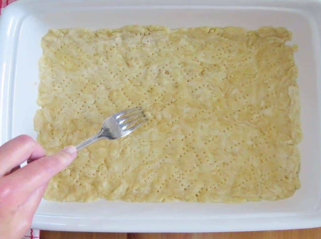 poking holes into the pie crust in the bottom of a baking dish
