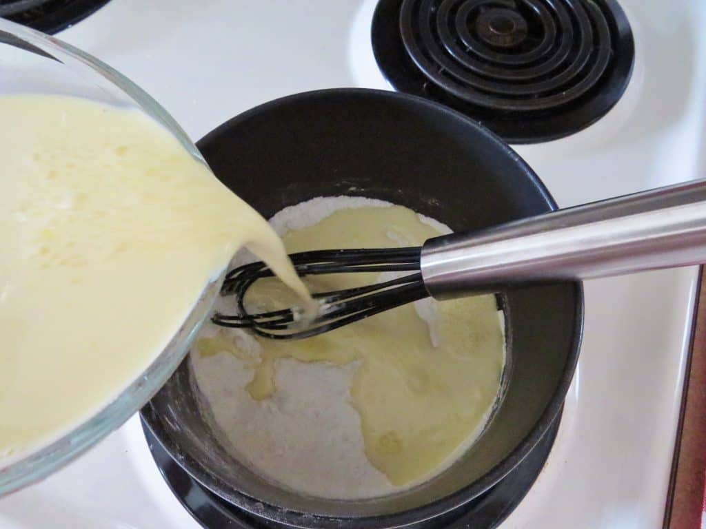 pouring heavy cream into a sauce pan with flour and sugar