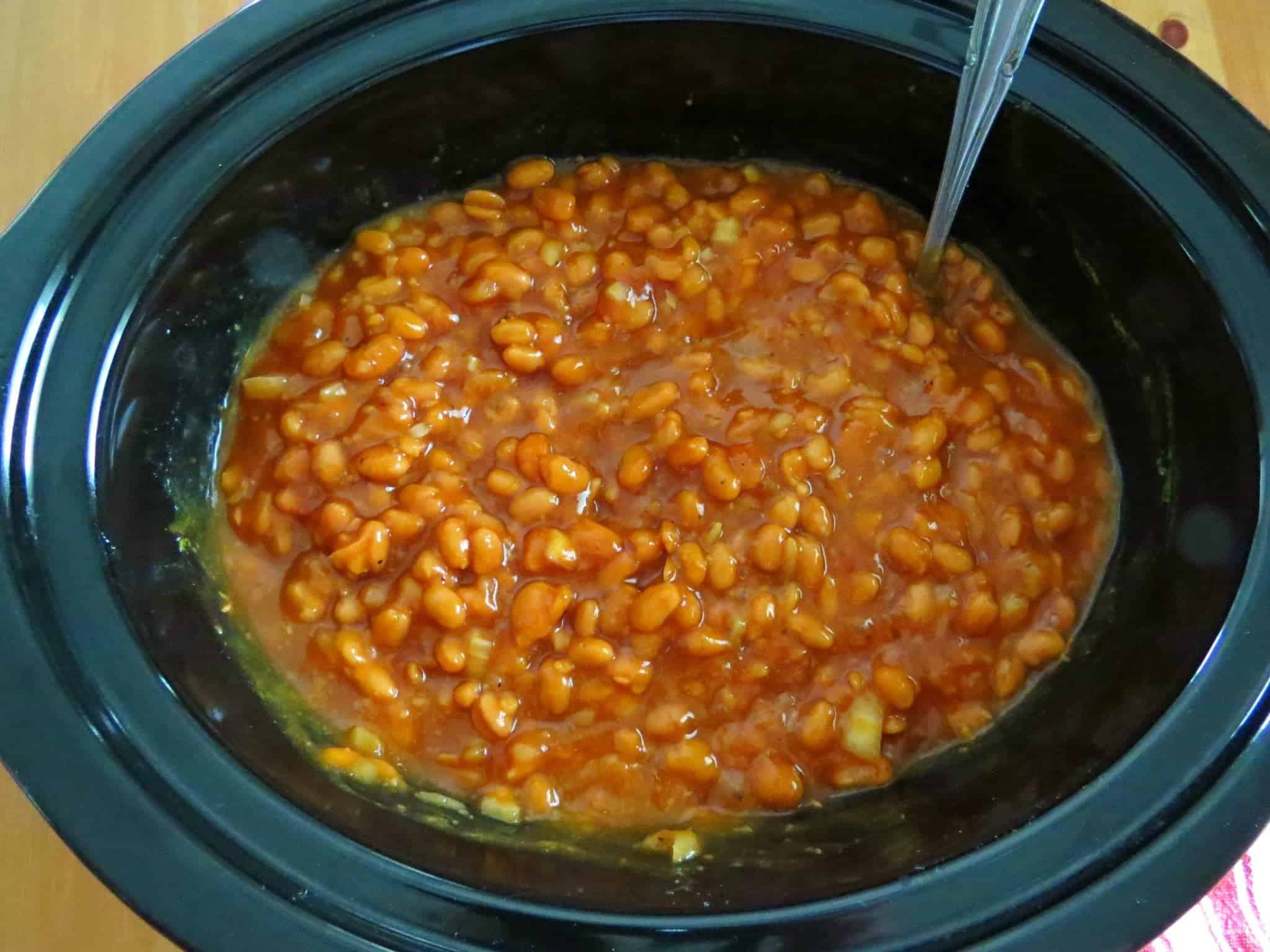 Baked Beans stirred in an oval crock pot with a spoon.
