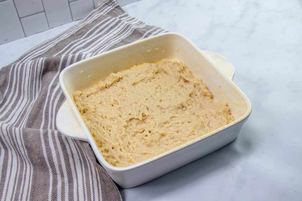 crumb cake batter spread into an white square baking dish.