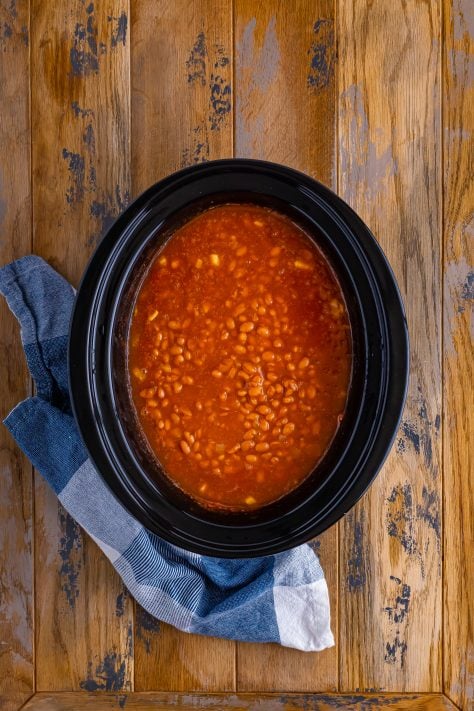 A stirred crock pot with baked beans.