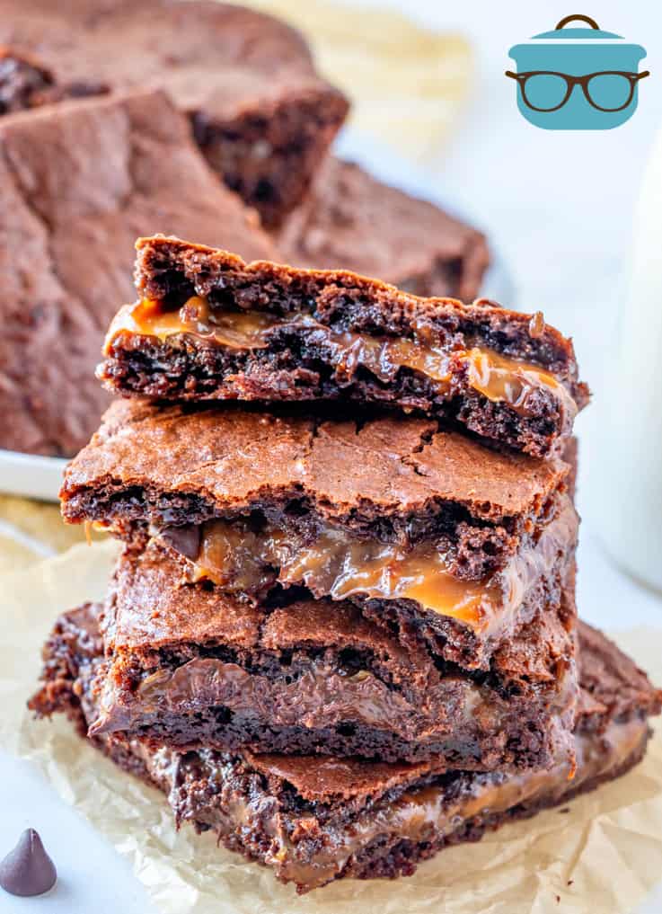 chocolate caramel layered brownies stacked on parchment paper.