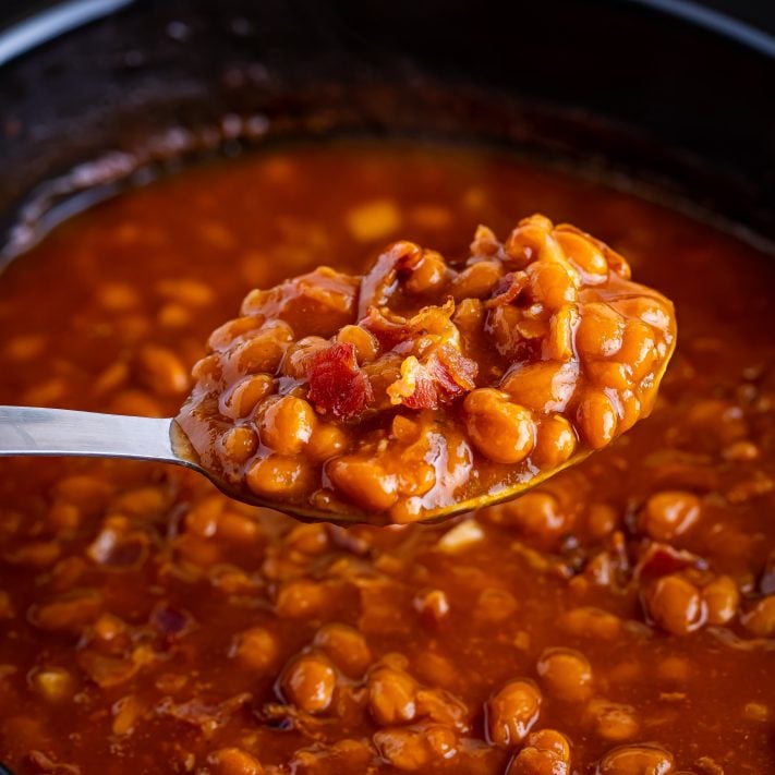 A spoon holding a scoop of Crock Pot Baked Beans over the Slow Cooker.