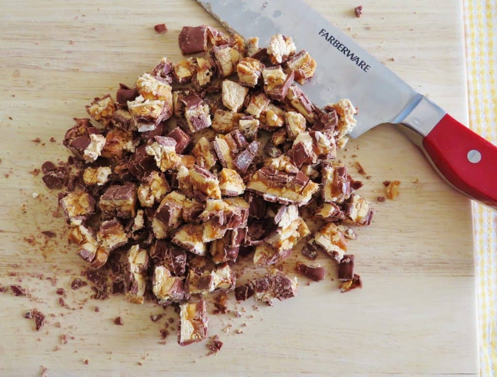 chopped Snickers candy bars on a wooden cutting board with a knife set to the side